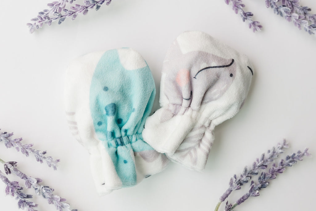 Polyester baby mittens with dinosaur characters next to fake purple leaves and a white background.
