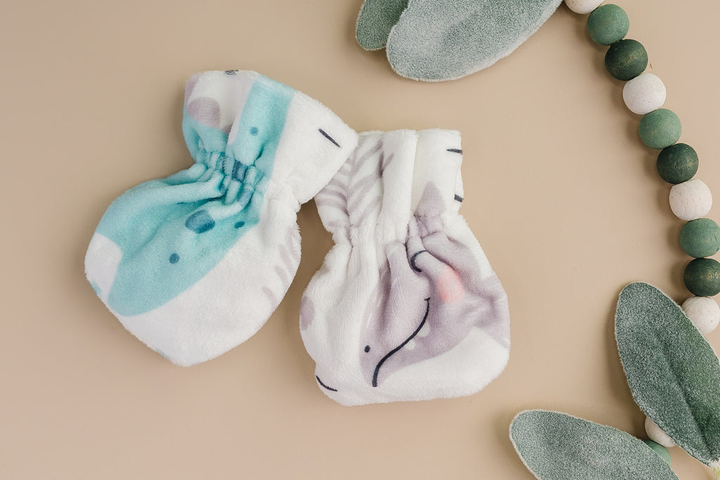 Polyester baby mittens with dinosaur characters next to fake leaves and green and white beads